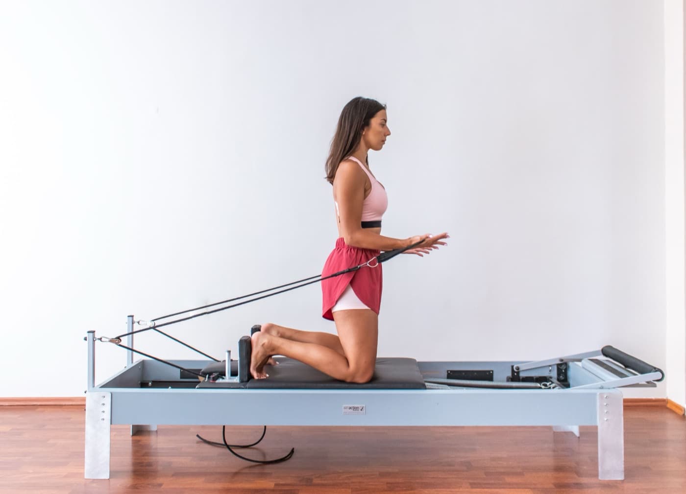 Woman kneeling on a pilates reformer holding the straps in a bright studio