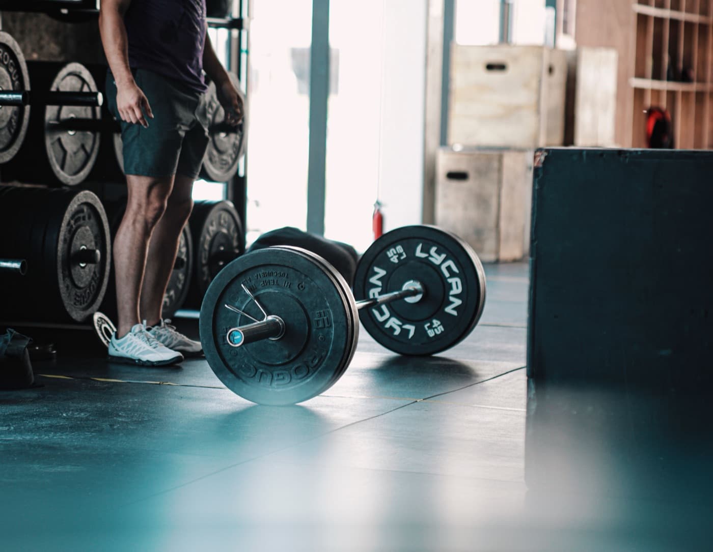 Loaded barbell on the floor of a CrossFit box, with bumper plates and plyo boxes behind it