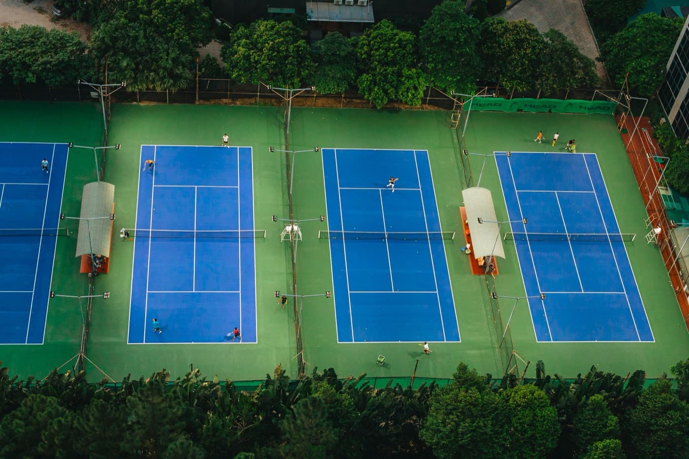 Aerial view of four blue tennis courts with players rallying