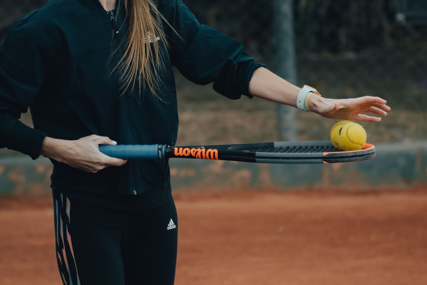 Tennis coach balancing two balls on a racket on a clay court
